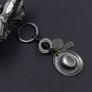 Vintage silver cowboy hat and gear keychain with leather strap on textured gray surface