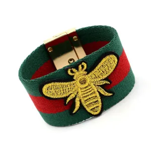 Détail d'un bracelet large en tissu rayé vert et rouge avec broderie d'abeille