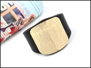 Macro detail of wide black pebbled leather cuff with embossed gold metal plate