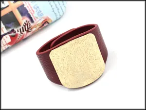 Macro detail of wine red pebbled leather bracelet with engraved gold metal plate decoration