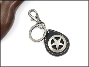 Detalle macro de un llavero de cuero vintage con estrella metálica y costura amarilla