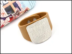 Macro shot of tan wide faux leather cuff featuring a hammered silver metal square plate