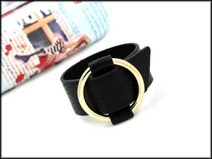Close-up of black lychee grain leather bracelet with a polished gold metal ring detail