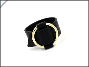 Detail of black lychee leather texture and large gold circular metal buckle on cuff bracelet