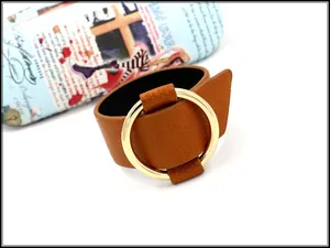 Detail of wide tan leather cuff bracelet featuring a large polished gold circular metal ring
