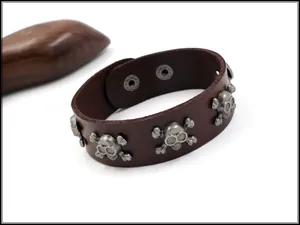 Close-up of brown punk leather bracelet featuring skull studs and adjustable metal snaps