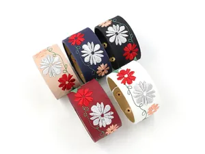 Detailed close-up of embroidered daisy patterns on colorful leather wide bracelets