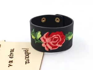 Détail d'un bracelet large en cuir noir avec broderie de rose rouge et boutons pression