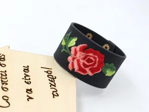 Détail d'un large bracelet en cuir PU noir avec broderie de rose rouge et boucle dorée