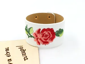 Détail d'un bracelet large en cuir PU blanc avec broderie de rose et boutons dorés