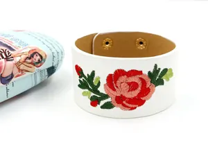 Detail eines weißen breiten PU-Lederarmbands mit roter Blumenstickerei und Druckknöpfen