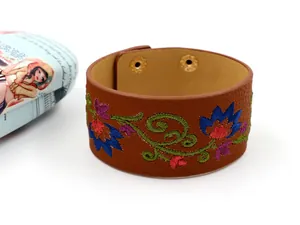 Primer plano del brazalete ancho de cuero PU marrón con bordado floral y broches metálicos