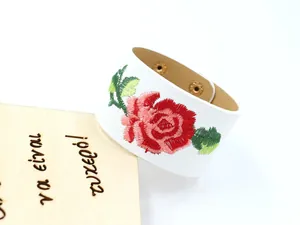 Gros plan sur bracelet en cuir PU blanc avec broderie rose rouge et boutons dorés