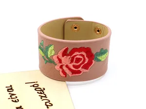 Gros plan d'un bracelet large en cuir PU rose avec broderie de rose et fermoirs dorés