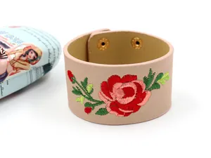 Detail der Blumenstickerei auf breitem rosa PU-Lederarmband mit goldenen Druckknöpfen