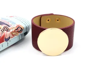 Detail of burgundy textured leather bracelet with a large golden circular alloy plate