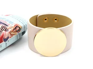 Detail of beige textured leather cuff bracelet featuring a large polished gold metal disc