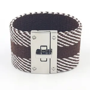 Detail van een brede geweven armband met bruin ruitpatroon en een zilveren metalen sluiting