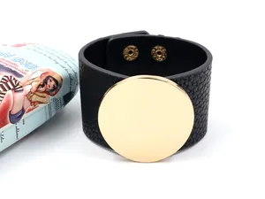 Detail of black pebbled leather cuff bracelet with large polished gold metal disk and snaps