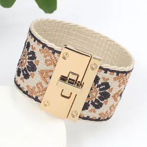Detail van een brede canvas armband met etnische patronen en een gouden metalen draaisluiting