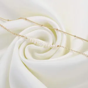 Detail of 18K gold plated steel chain bracelet with small white pearls on white silk