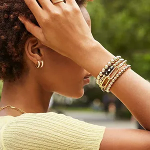 Detailed view of layered 18K gold-plated bead bracelets with charms on a female wrist
