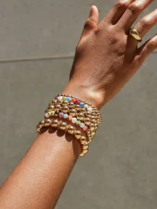 Detail of stacked 18K gold bead bracelets with floral accents and a polished ring