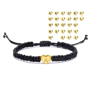 Detail of black woven rope bracelet featuring a golden heart bead with letter A engraving