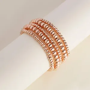 Macro detail of five-piece rose gold beaded elastic bracelets on a white display stand