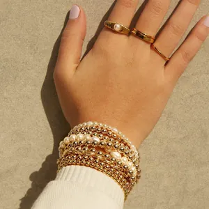Detail of 18K gold beaded bracelets and stacked rings worn by a model in soft light