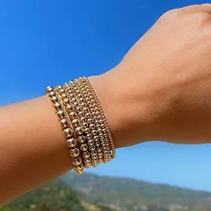 Detail of stacked gold beaded bracelets with blue evil eye charm against a sky backdrop