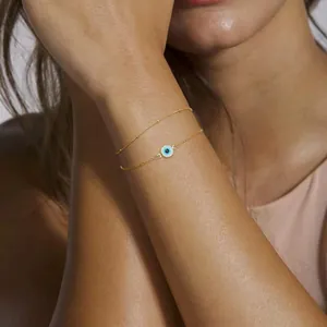 Detail of 18K gold stainless steel layered chain bracelet with blue evil eye charm