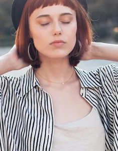 Close-up of a delicate 18K gold chain with a single pearl and large silver hoop earrings
