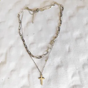 Macro detail of a double-layered stainless steel necklace featuring a cross pendant and clasp