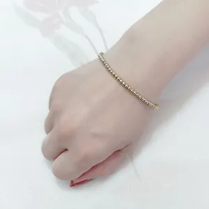Detail showing the polished 18K gold beaded bracelet worn on a wrist for size comparison