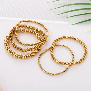 Detail of stacked golden stainless steel bead bracelets with blue evil eye charms