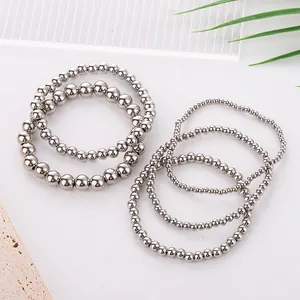 Detailed stack of six polished stainless steel bead bracelets on a modern stone base