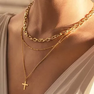 Detail of layered gold cross necklace with beaded chain and curb chain on a model