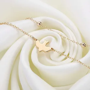 Detailed macro of a 18K gold plated stainless steel bird charm on a layered chain