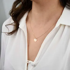 Detail of 18K gold-plated necklace featuring a round pendant with engraved letter L