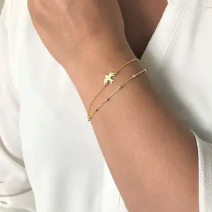 Close-up of double-layer gold chain bracelet with swallow charm on a woman wrist