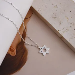 Macro shot of silver David Star pendant on cross chain atop a beige travertine stone