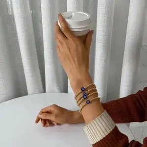 Detail of four gold bead evil eye bracelets layered on a wrist holding a coffee cup