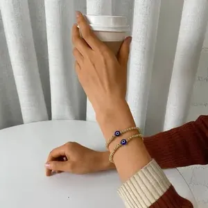 Detail of two-piece golden beaded bracelets featuring blue evil eye charms on a wrist