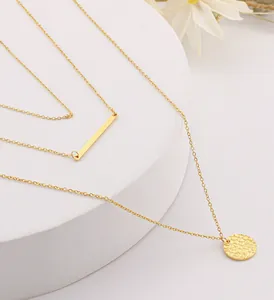 Detail of layered gold-plated chain necklace featuring bar and hammered disc pendants