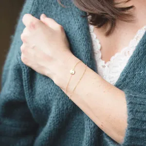 Detail of a minimalist gold layered chain bracelet with coin pendant on a model's wrist