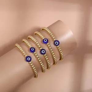 Five-piece gold beaded evil eye charm bracelet set on a cylindrical jewelry display stand