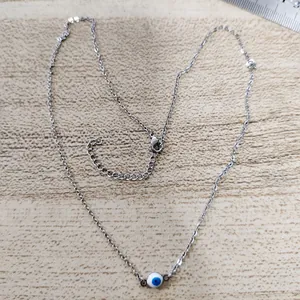 Detail of silver stainless steel evil eye necklace with blue bead on wooden surface