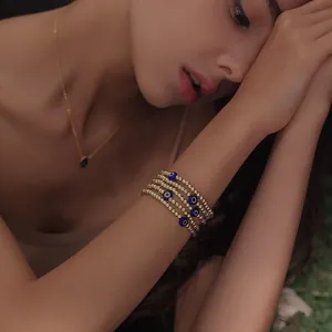 Detailed view of layered gold beaded bracelets with blue evil eye charms on wrist