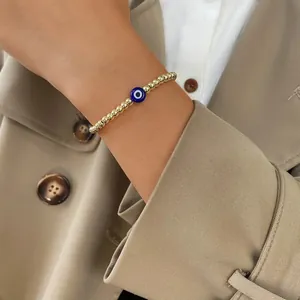 Detail of gold beaded bracelet featuring a blue evil eye charm worn on a female wrist